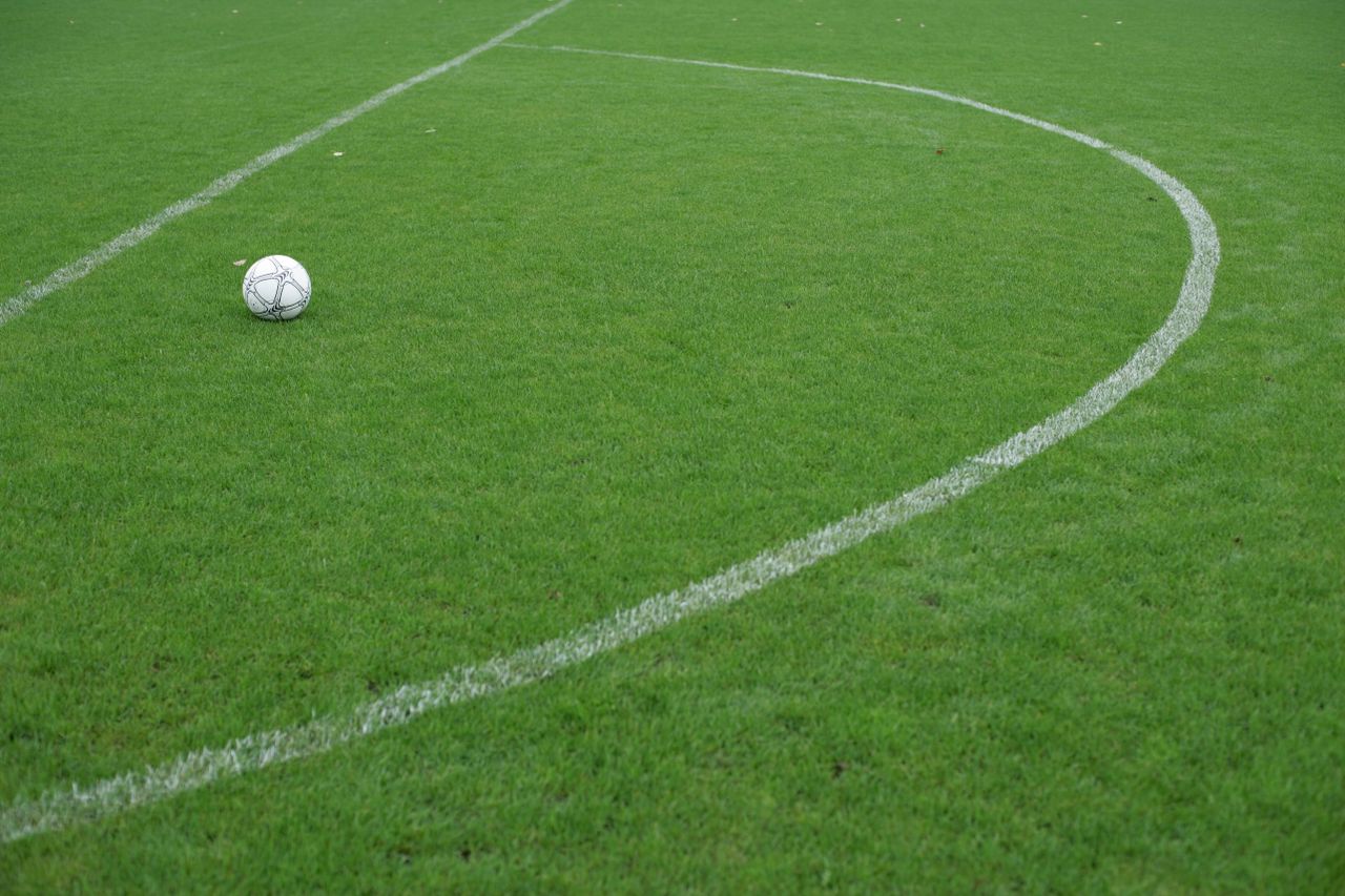 why-choose-us-02 Soccer ball resting on a vibrant green field with white boundary lines.